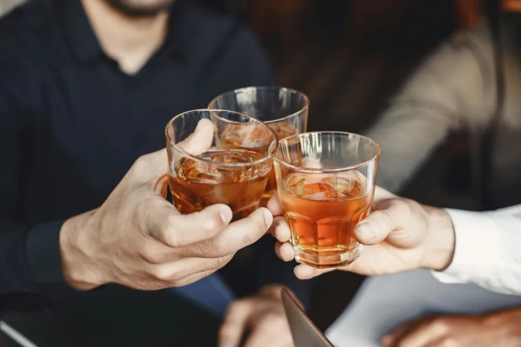 Hands of three men holding alcoholic drinks, symbolizing social drinking—a habit that may worsen prostate-related health issues.
