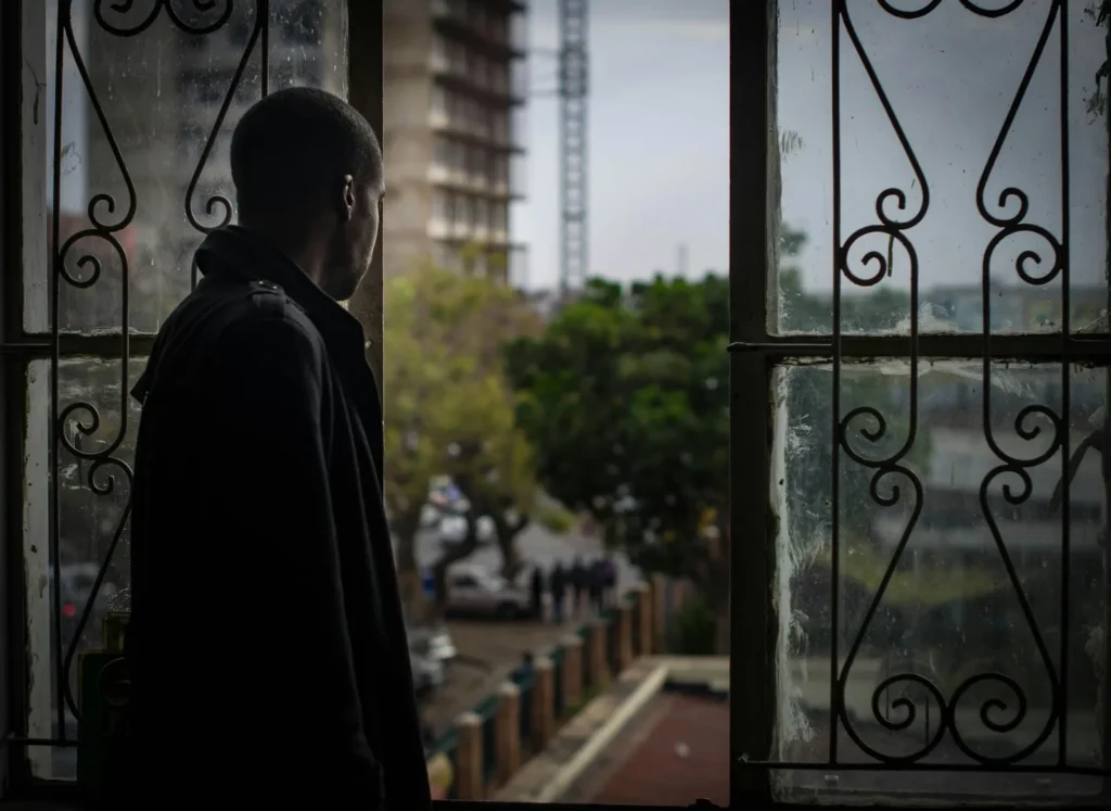Man gazing out of a window with a thoughtful expression, symbolizing concern or reflection about health issues like BPH and prostate cancer.