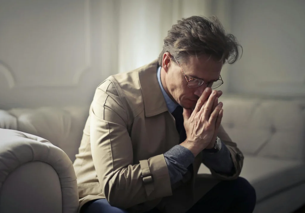 Middle-aged man sitting with a worried expression, hands on his face or knees, reflecting anxiety or concern about urinary or prostate health issues.