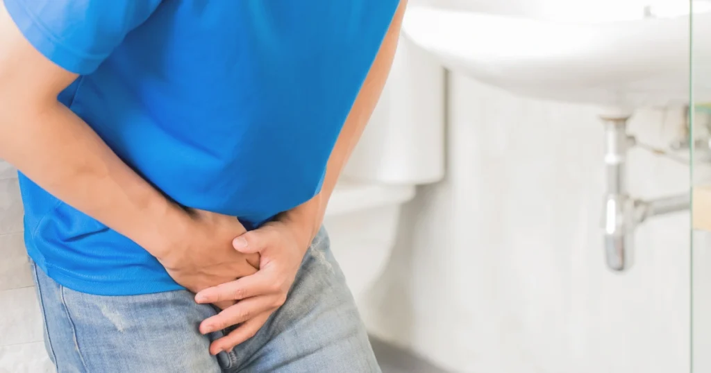 Man placing his hand over his lower abdomen or groin area, indicating discomfort or urgency, commonly associated with prostate or urinary issues.